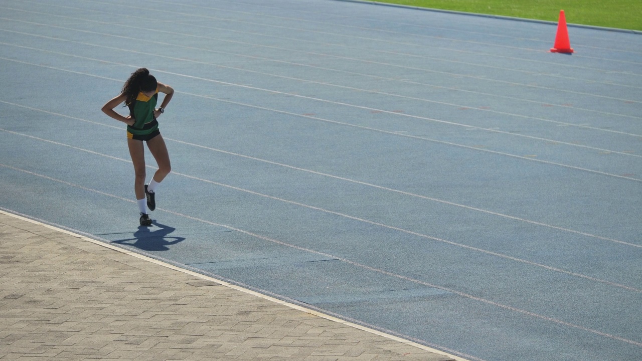 女田径运动员在阳光明媚的蓝色跑道上练习视频素材