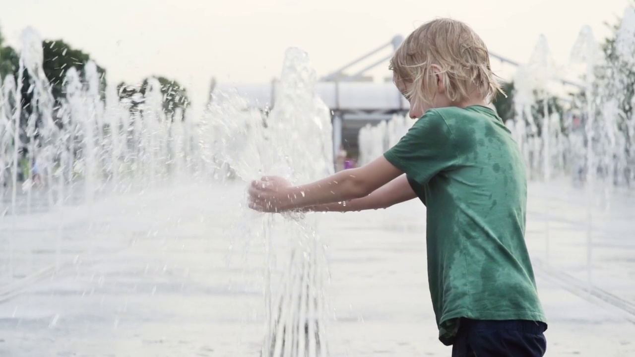 一个阳光明媚的夏日，小男孩在城市喷泉的喷泉之间的广场上玩耍。城市孩子们活跃的夏季休闲活动。视频素材
