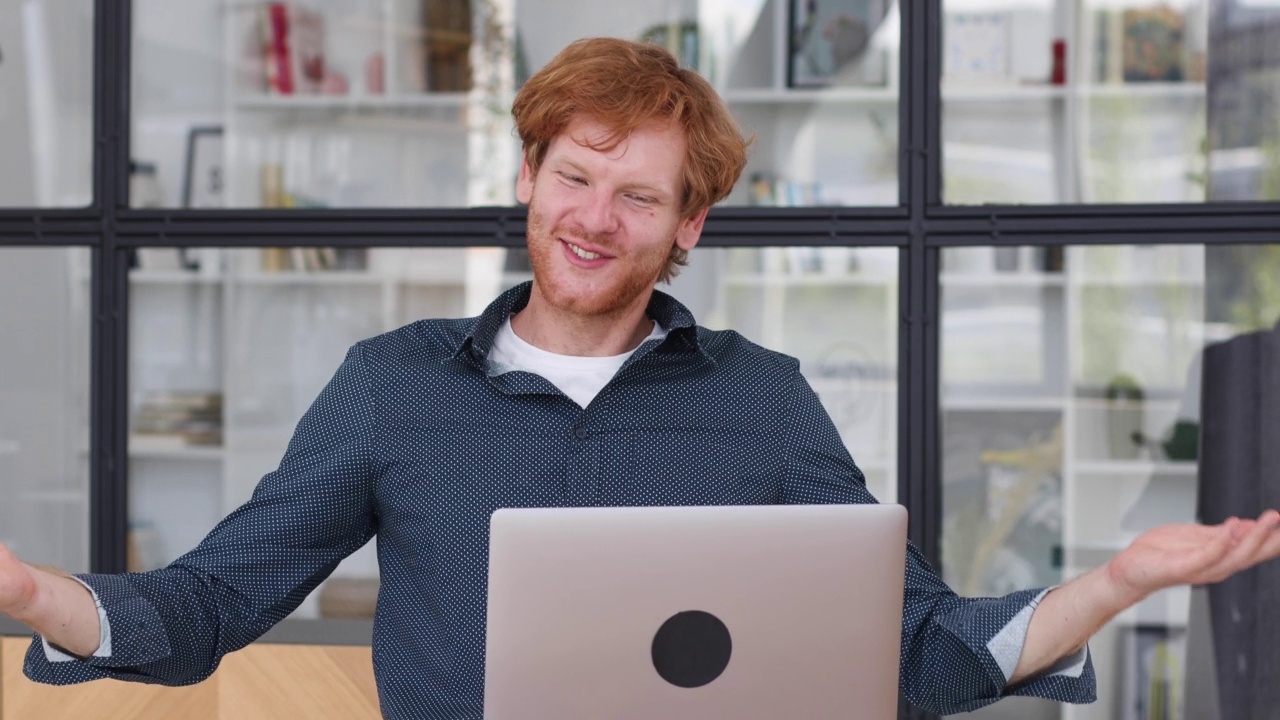 年轻的白人红发男性办公室职员，使用笔记本电脑进行视频通话坐在工作场所。在线会议，视频通话视频素材