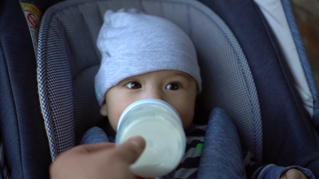 婴儿车里的婴儿用奶瓶吸奶。一个新生儿在走路时吃东西的特写镜头。视频素材