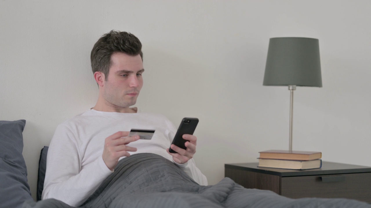 男人在床上用智能手机在线支付视频素材