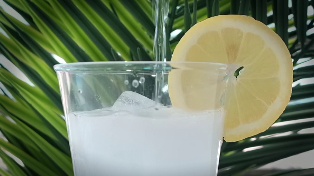 将苏打水倒入杯中，以棕榈叶为背景，加入冰块视频下载