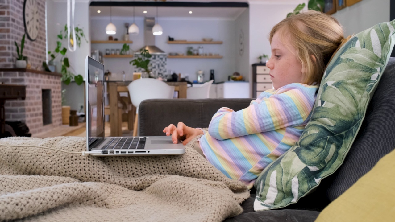 年轻的女孩在家里的沙发上使用笔记本电脑视频下载
