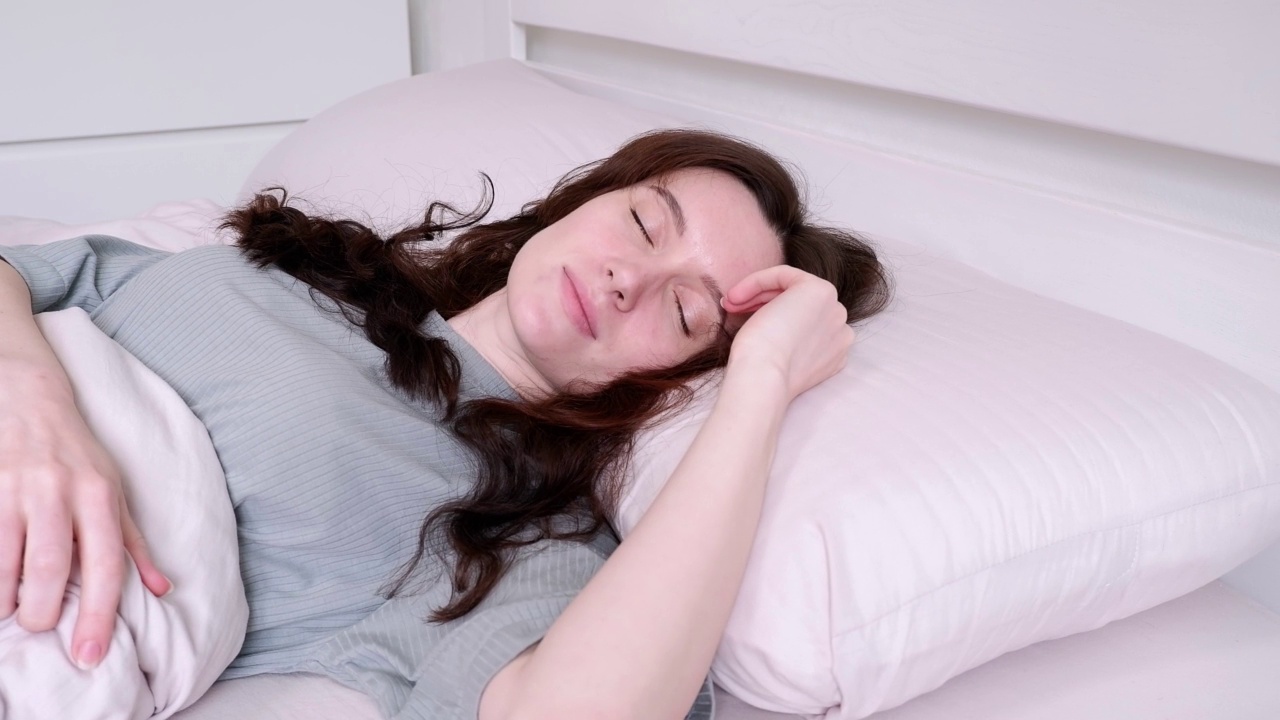 微笑的女人倒在枕头上睡着了。漂亮明亮的现代风格的房间视频素材