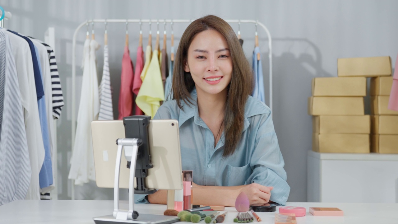 亚洲女人的肖像在网上卖衣服和看着相机。有吸引力的美丽的年轻女商人坐在桌子上自信和感觉快乐的金融业务在仓库视频下载