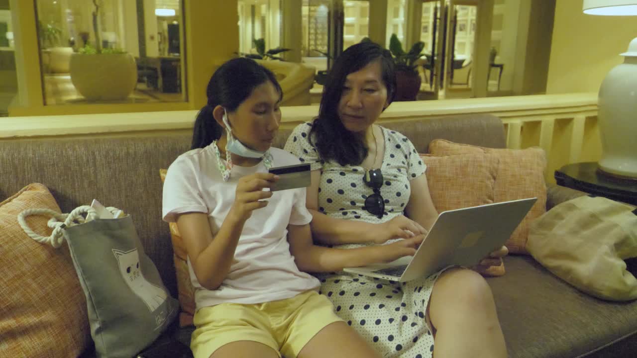 亚洲女孩帮助她的母亲阅读信用卡号码购物或在线预订一起。视频素材
