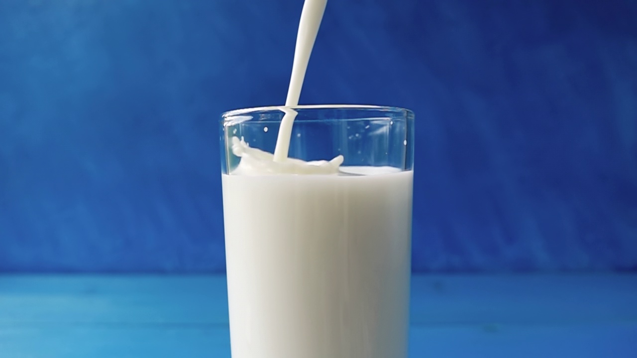 牛奶倒进一个杯子与美丽的飞溅特写蓝色模糊的背景。4 k原始视频。用高速电影摄影机拍摄的。视频素材