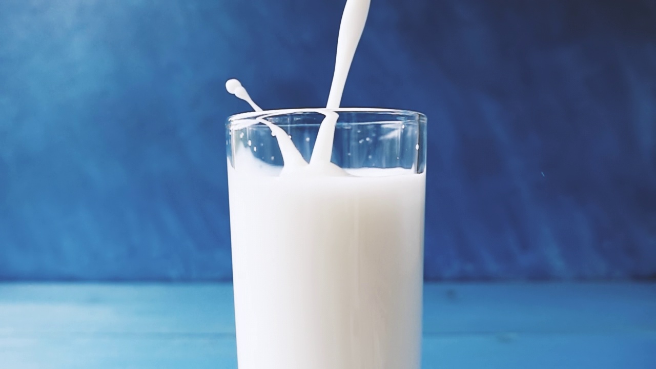 牛奶倒进一个杯子与美丽的飞溅特写蓝色模糊的背景。4k原始视频60帧/秒。用高速电影摄影机拍摄的。视频素材