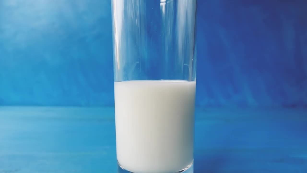牛奶倒进一个杯子与美丽的飞溅特写蓝色模糊的背景。4k原始视频60帧/秒。用高速电影摄影机拍摄的。视频素材