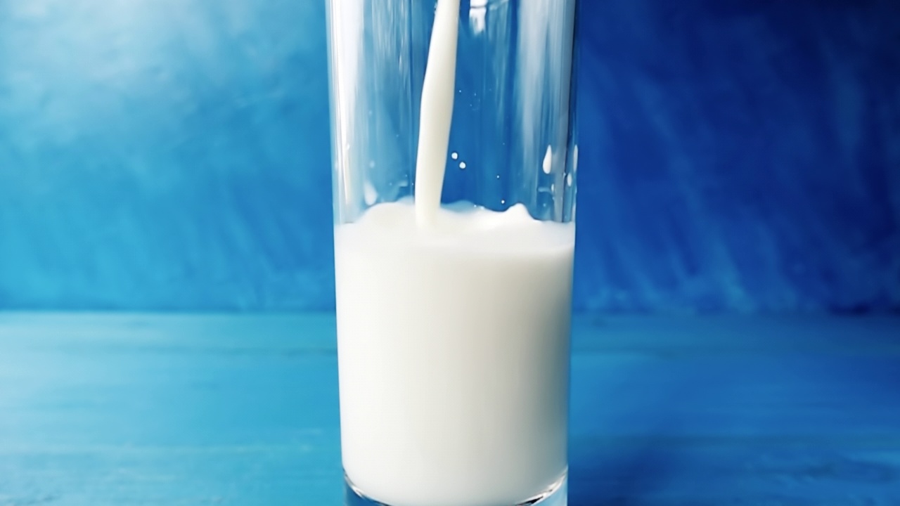 牛奶倒进一个杯子与美丽的飞溅特写蓝色模糊的背景。带有速度斜坡效果的4k原始视频。用高速电影摄影机拍摄的。视频素材
