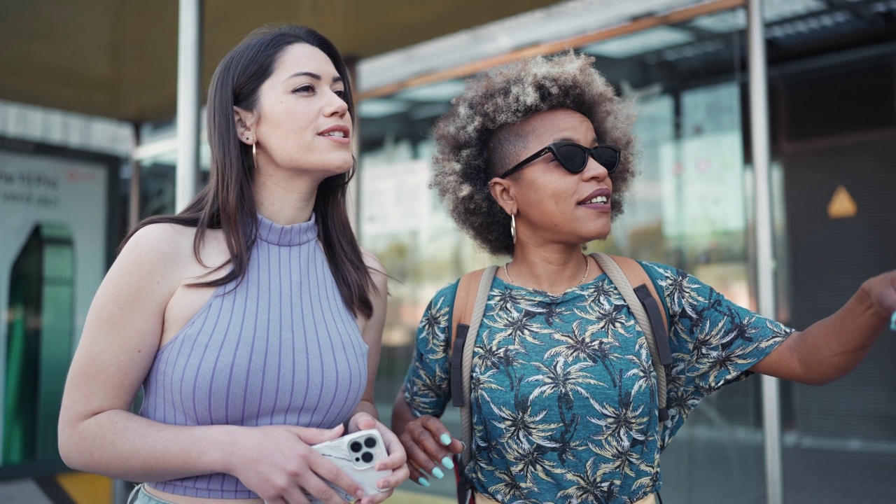 两个英俊的多民族女人在公共汽车站边聊天边叫出租车视频素材