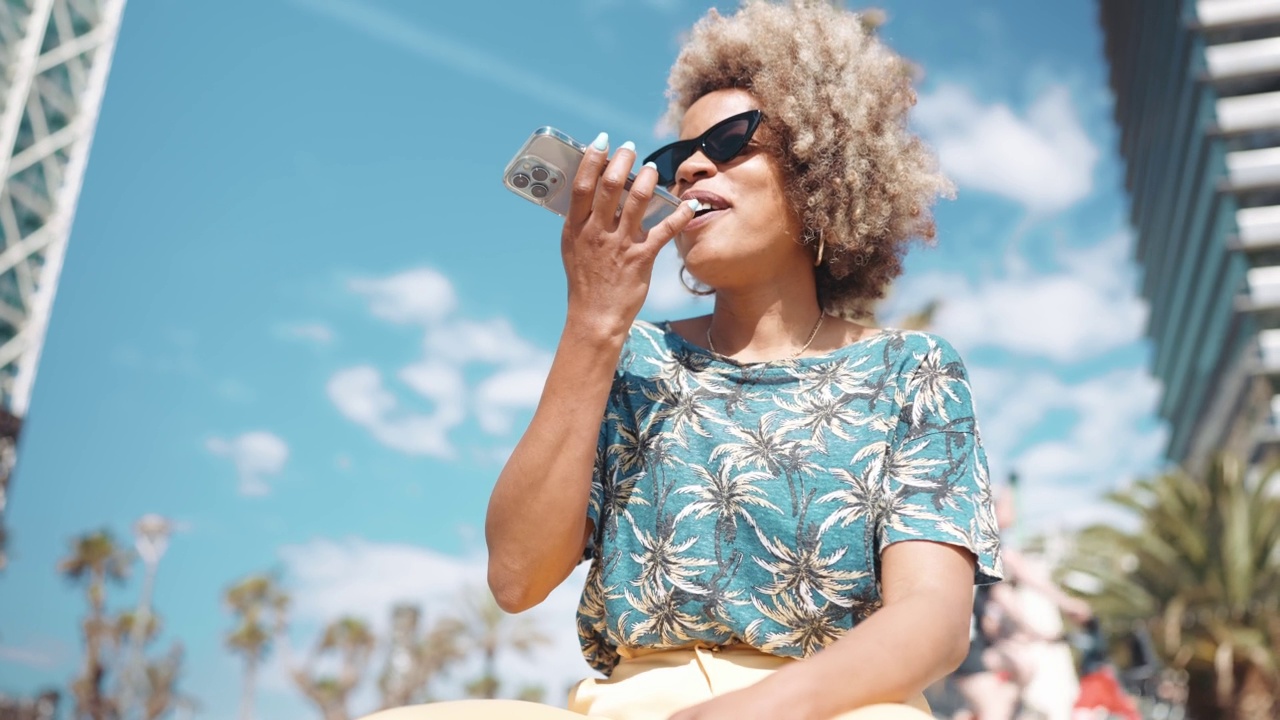 快乐的非洲灰色头发的女人戴着太阳镜录音语音信息的手机视频素材