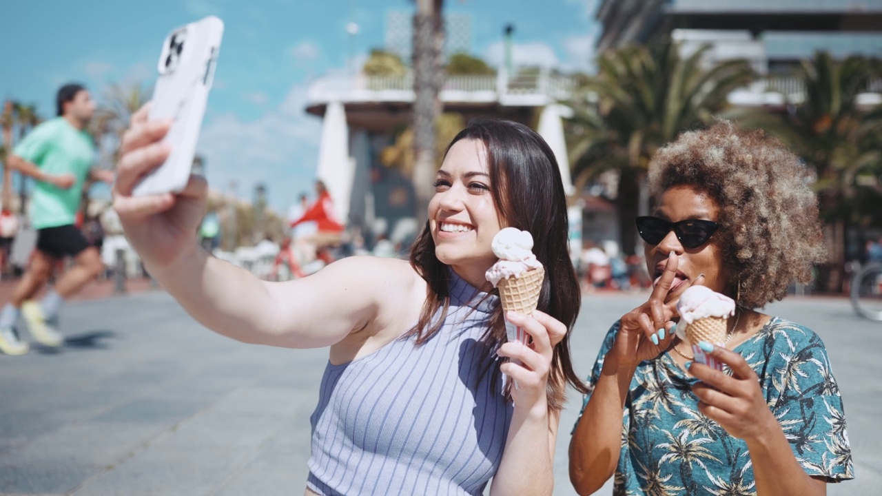 两名微笑的多民族女性在手机相机上与冰淇淋自拍视频素材