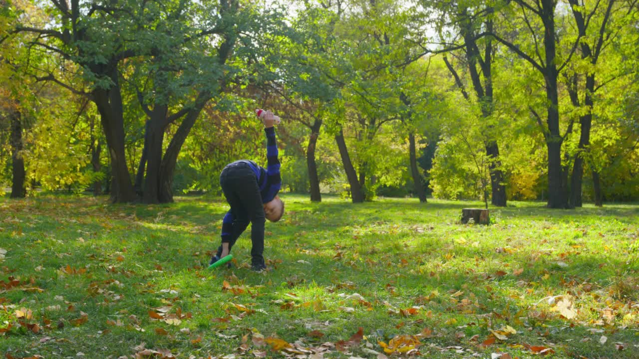 初中男孩在温暖的休闲服装与狗玩具的乐趣秋天公园郁郁葱葱的树木和黄色的叶子在阳光明媚的天气视频下载