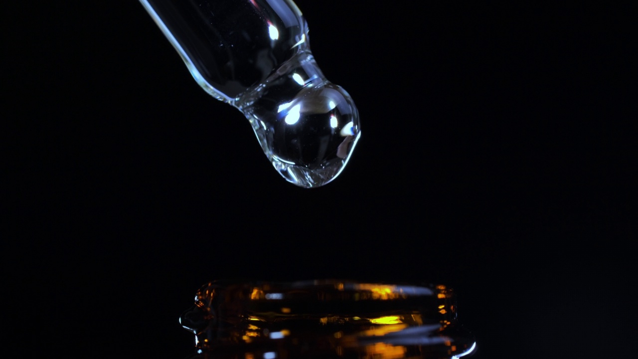 黑色背景下化妆品油从吸管滴进瓶子的特写。视频素材