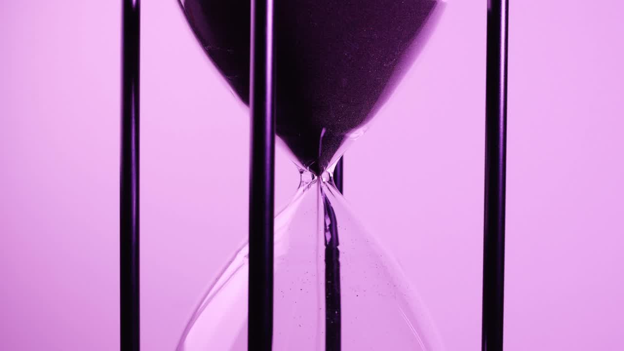 特写的沙子计时器时钟与沙子流动从沙漏在紫色色调。视频素材
