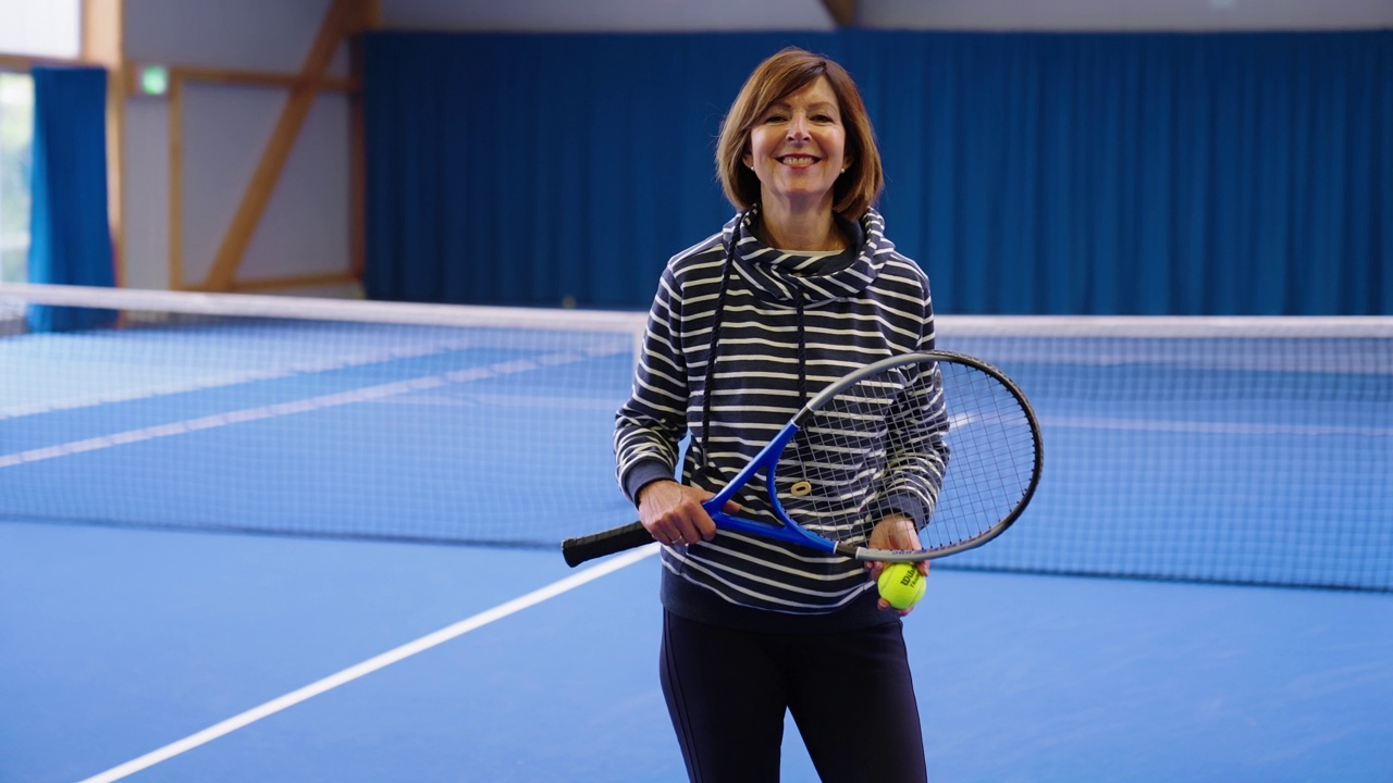 一个健康成熟的女人站在网球场上的肖像。视频素材