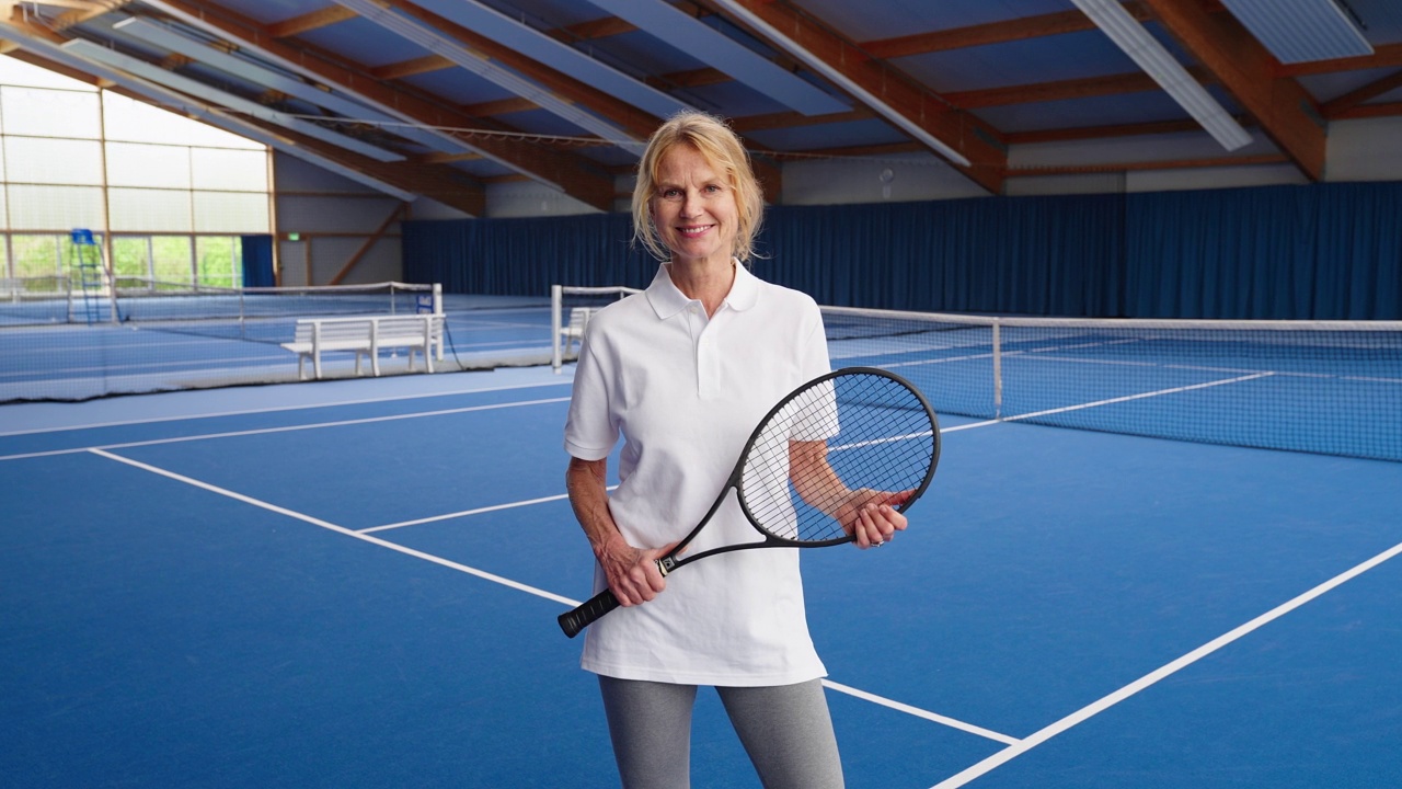 一个微笑的成熟女人的肖像与球拍站在网球场上视频素材