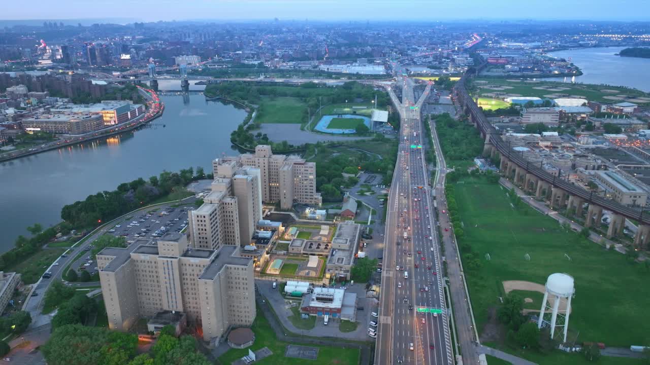 高速公路上有很多交通工具经过。无人机在城市上空拍摄了绿色公园、河流和体育场。日落时分的纽约。视频素材