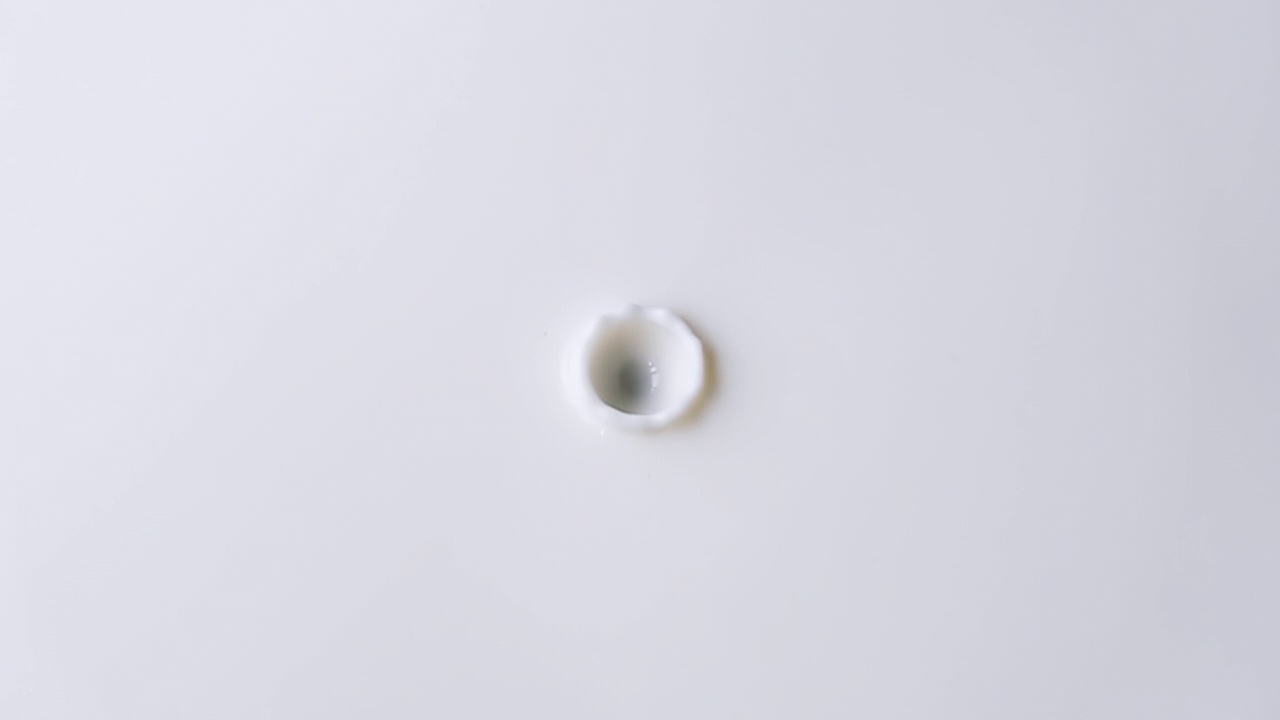 牛奶滴从顶部到中心在一个固体表面的牛奶特写。牛奶滴下的背景。4k原始慢动作视频60帧/秒。用高速电影摄影机拍摄，1000帧/秒。视频素材