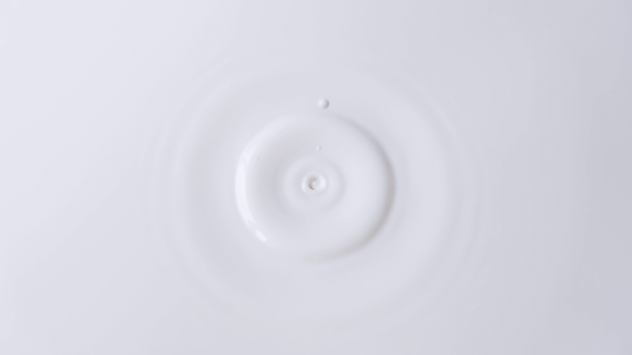 牛奶滴从顶部到中心在一个固体表面的牛奶特写。牛奶滴下的背景。带有速度斜坡效果的4k原始慢动作视频。用高速电影摄影机拍摄，1000帧/秒。视频素材
