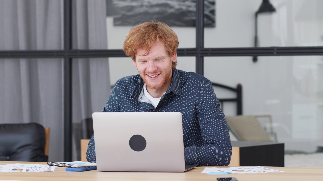 年轻的白人红发男性企业家或办公室职员使用笔记本电脑与坐在工作场所的员工或合伙人进行视频会议视频下载