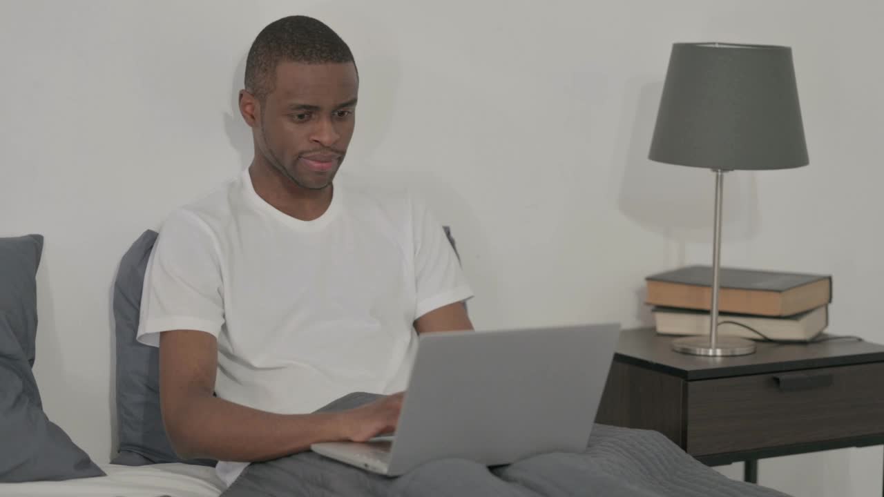 使用笔记本电脑的非洲男子在床上头痛视频素材