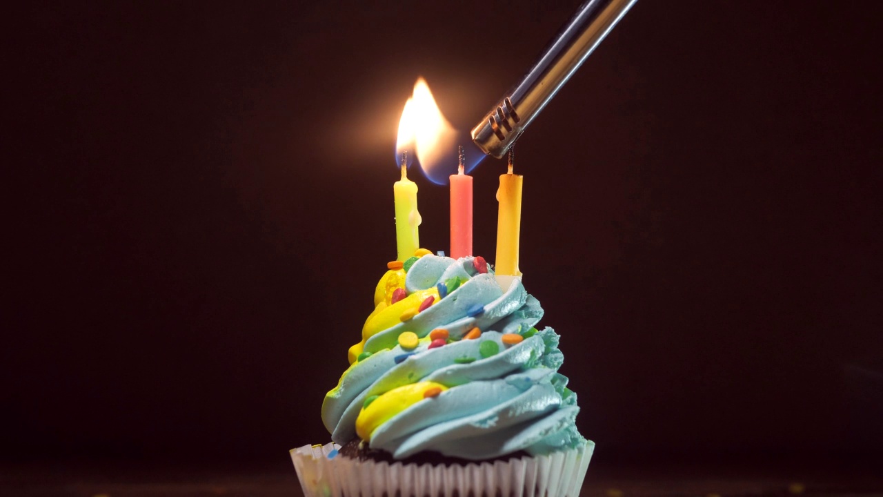 木桌上放着一个生日纸杯蛋糕，上面有蓝黄相间的奶油糖霜和点燃的蜡烛。副本的空间。文本的地方视频素材