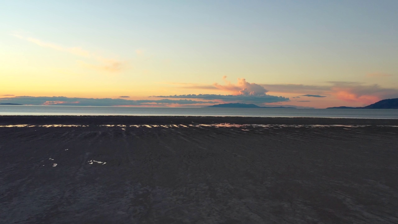 无人机在日落时飞过沙滩飞向湖泊视频下载