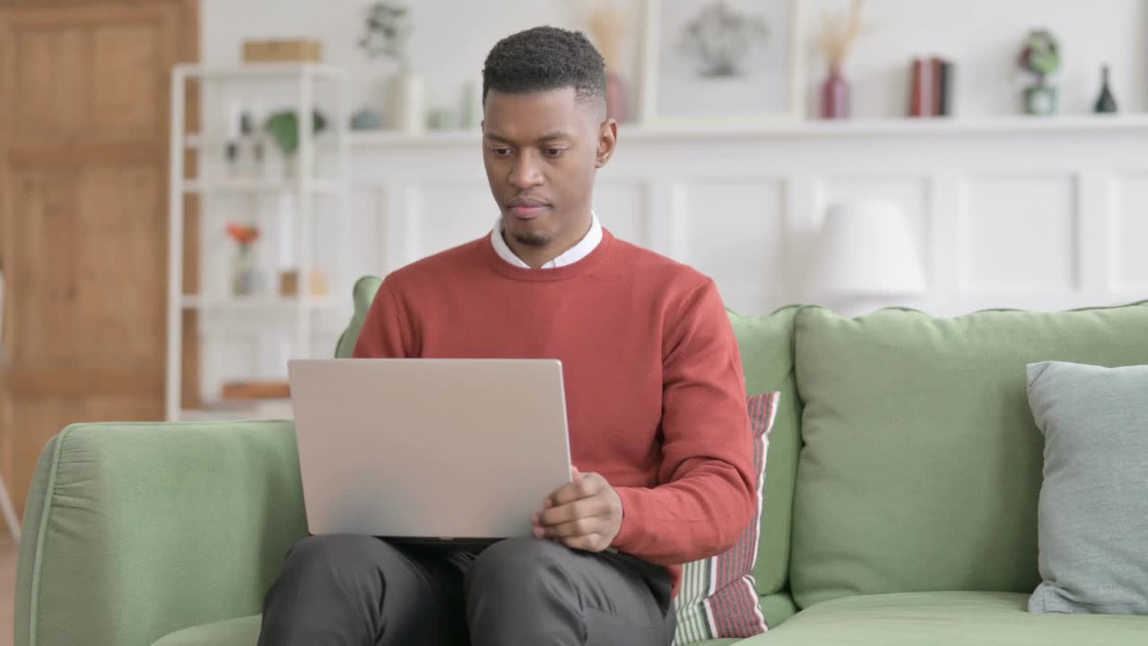 拿着笔记本电脑的非洲人坐在沙发上头痛视频素材