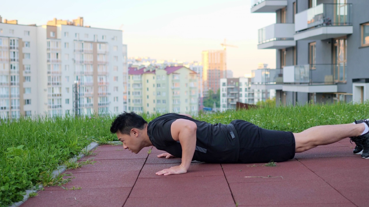 在城市建筑背景下，亚洲人在户外锻炼的侧面视图。男子肖像做俯卧撑在运动场地在睡眠区镇。运动员在户外锻炼。视频下载