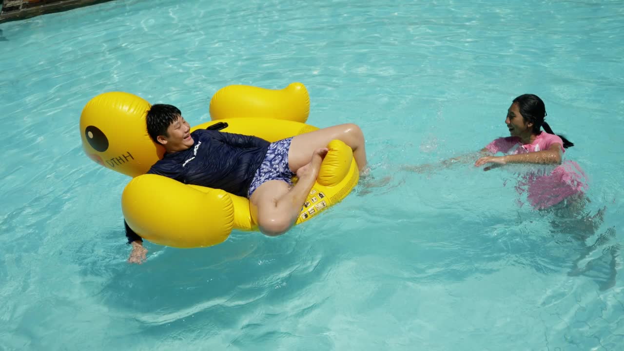 快乐的亚洲孩子在酒店或度假村与家人一起在泳池里玩黄鸭橡皮艇，生活理念。视频素材