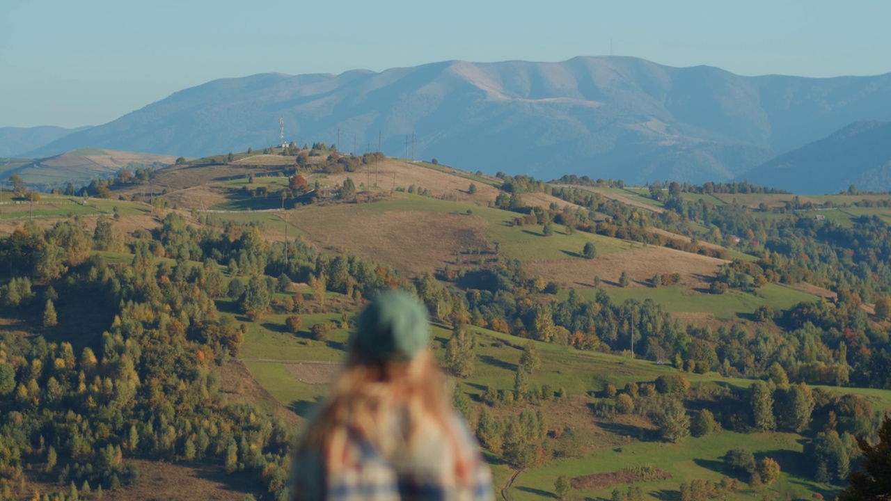 女徒步旅行者在美丽的黄色风景前走在草坡上。年轻的女性走在山顶上的绿色草地在阳光明媚的秋天傍晚。雄伟的秋山景观视频素材