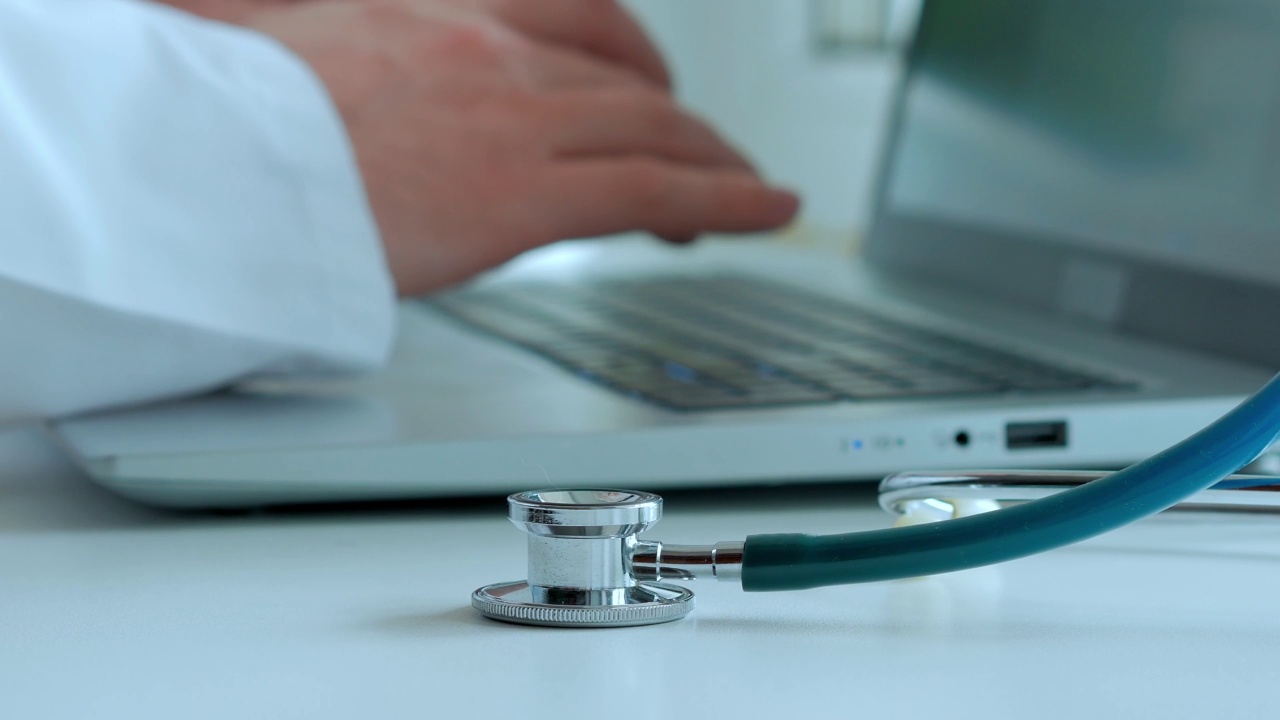 一个穿着白袍的医生的手在笔记本电脑的键盘上打印一段文字，前景的焦点，选择性的焦点视频素材