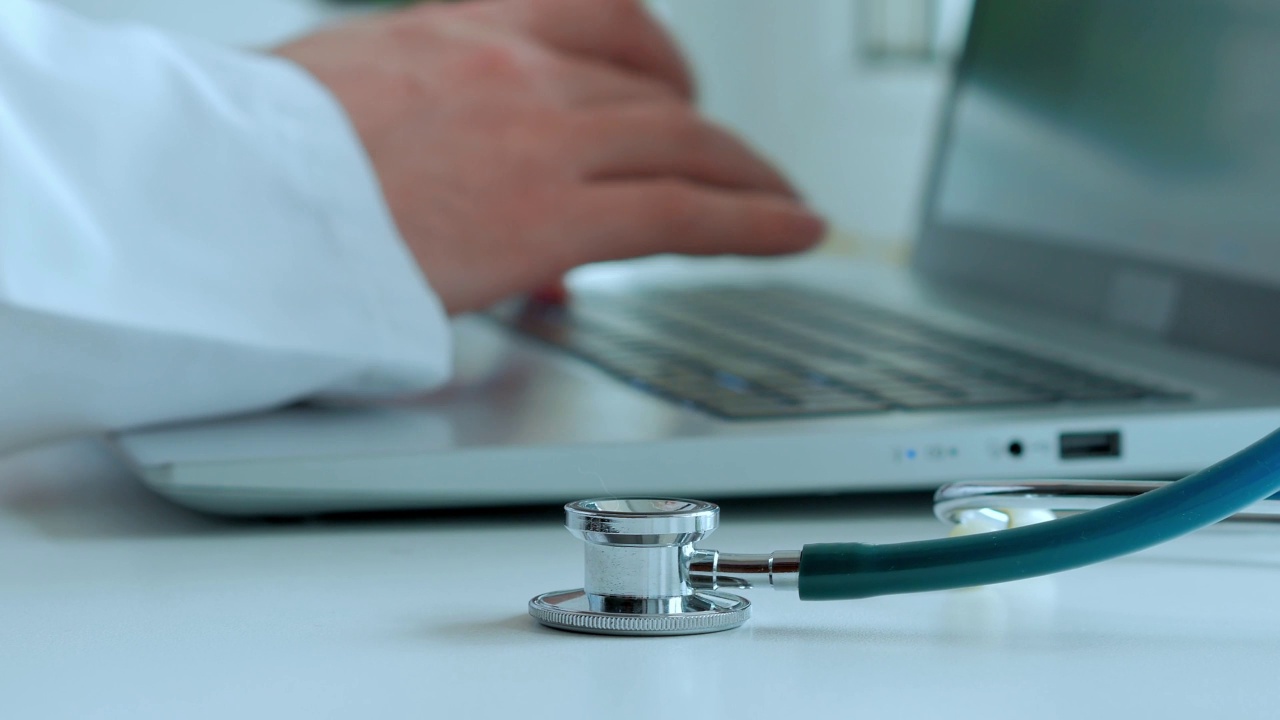 概念医学，医生工作，一名白大褂男子的手在笔记本电脑上打印文字，一个风扇内窥镜放在白色的桌子上视频素材