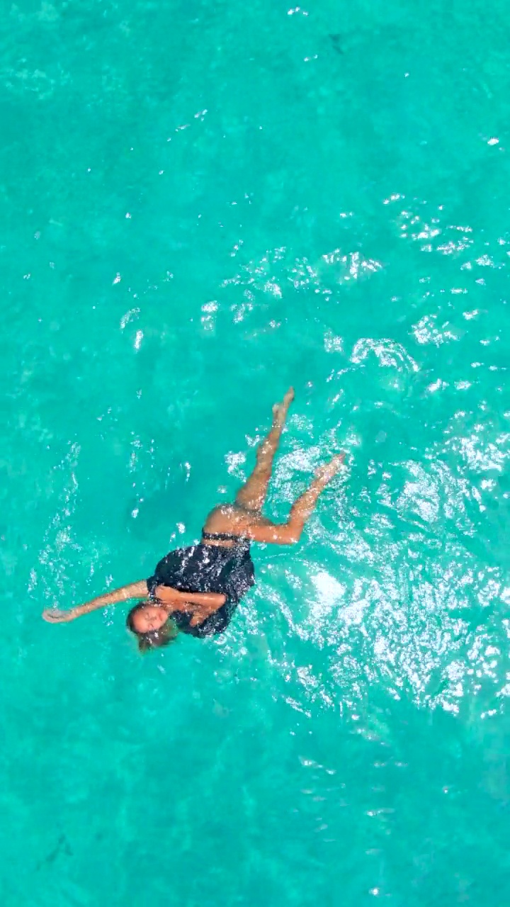 女子游泳比基尼和披风在风景优美的热带岛屿在水上平房酒店度假村，空中无人机的看法。- - - - - -垂直格式视频下载