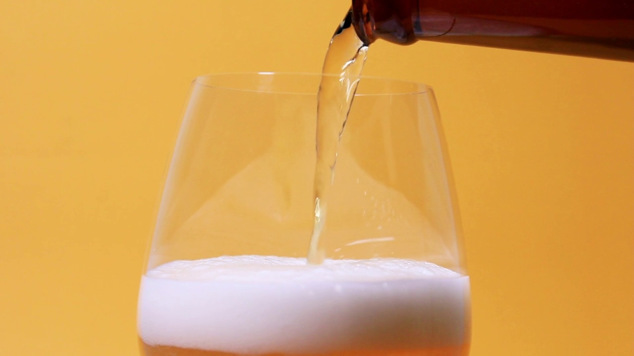 倒啤酒到玻璃从瓶子到顶部特写视图的黄色背景视频素材