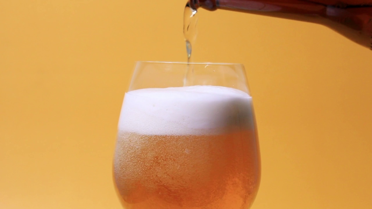 倒啤酒的慢动作从瓶子到玻璃顶部的特写角度上黄色风格视频素材