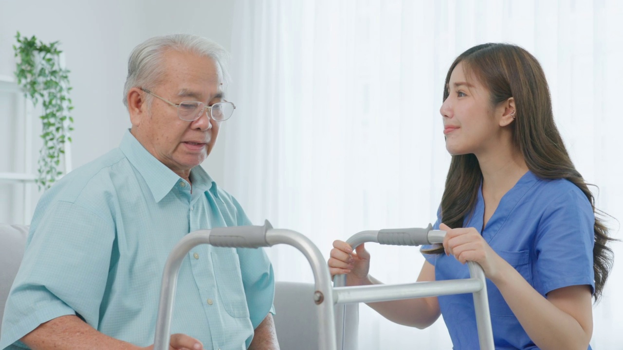 亚洲老年男性病人做物理治疗与照顾者。有吸引力的专业护理妇女帮助和支持年长的成熟男性实践行走缓慢与步行者在养老院照顾。视频素材