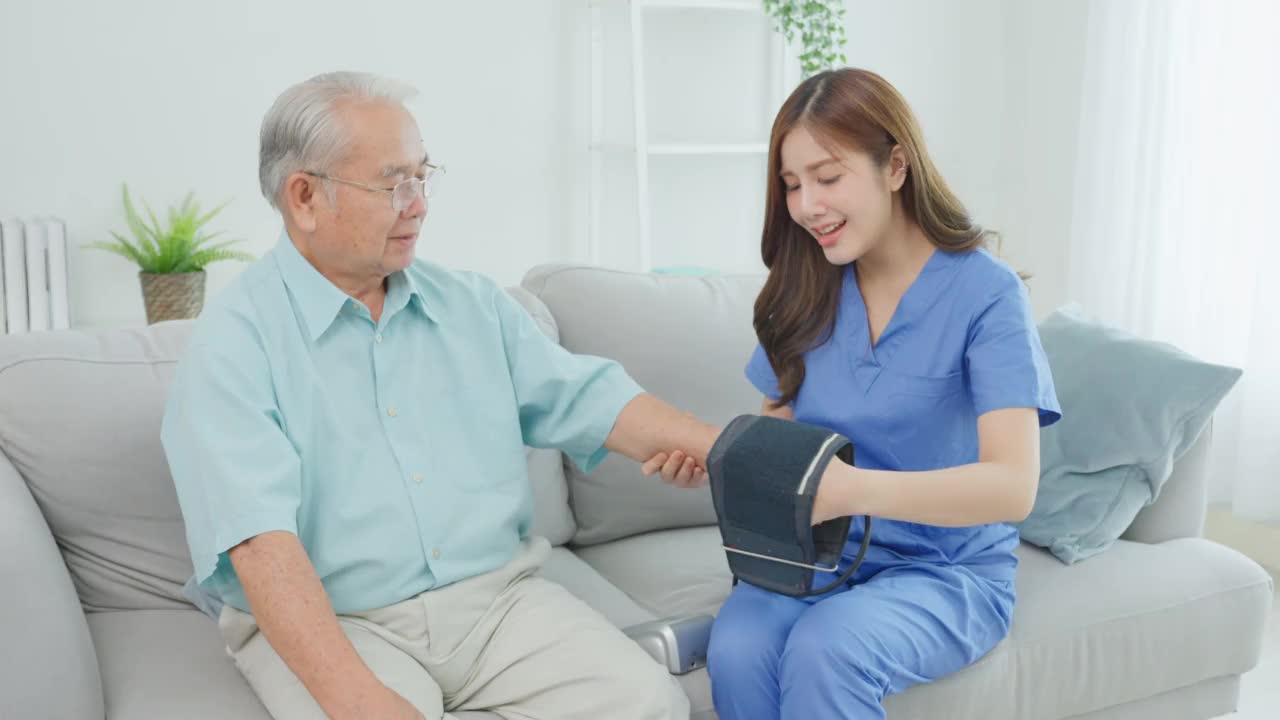 亚洲美女护理护士在老年男性病人身上使用血压计。迷人的美丽的医疗治疗师医生坐在家里的沙发上检查老年男性的健康视频素材