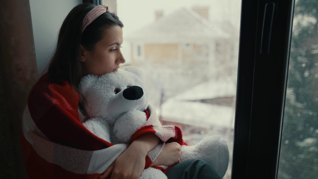 抱着泰迪熊坐在窗台上的女人视频素材
