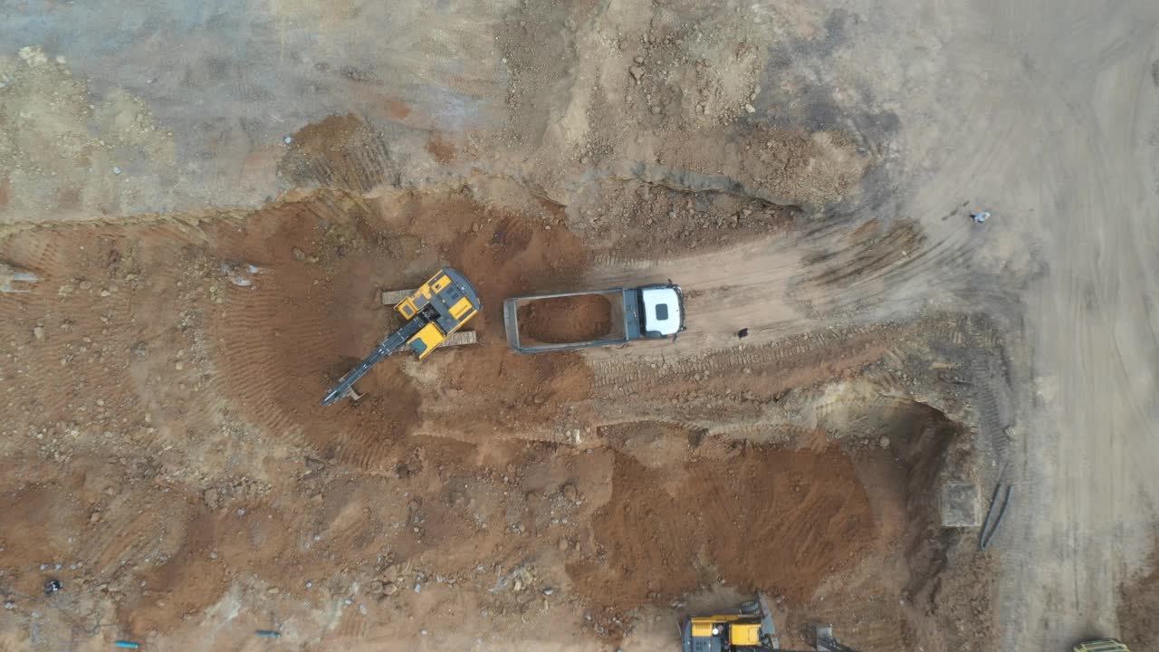 航拍现场采矿场地。无人机飞过挖土机挖土并将土装载到自卸卡车上。建筑施工中的土方搬运设备。重工业的概念。俯视图视频素材