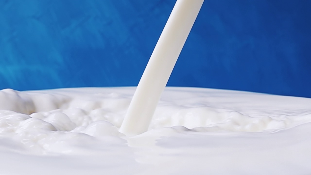 牛奶倒在牛奶表面的特写与美丽的飞溅和滴在蓝色的背景。4k原始慢动作视频。用高速电影摄影机拍摄，1000帧/秒。视频素材