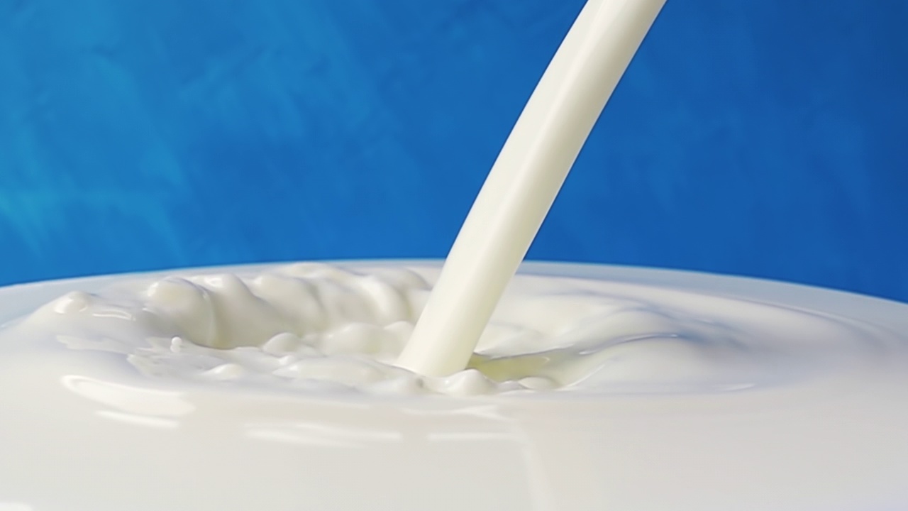 牛奶倒在牛奶表面的特写与美丽的飞溅和滴在蓝色的背景。带有速度斜坡效果的4k原始慢动作视频。用高速电影摄影机拍摄，1000帧/秒。视频素材