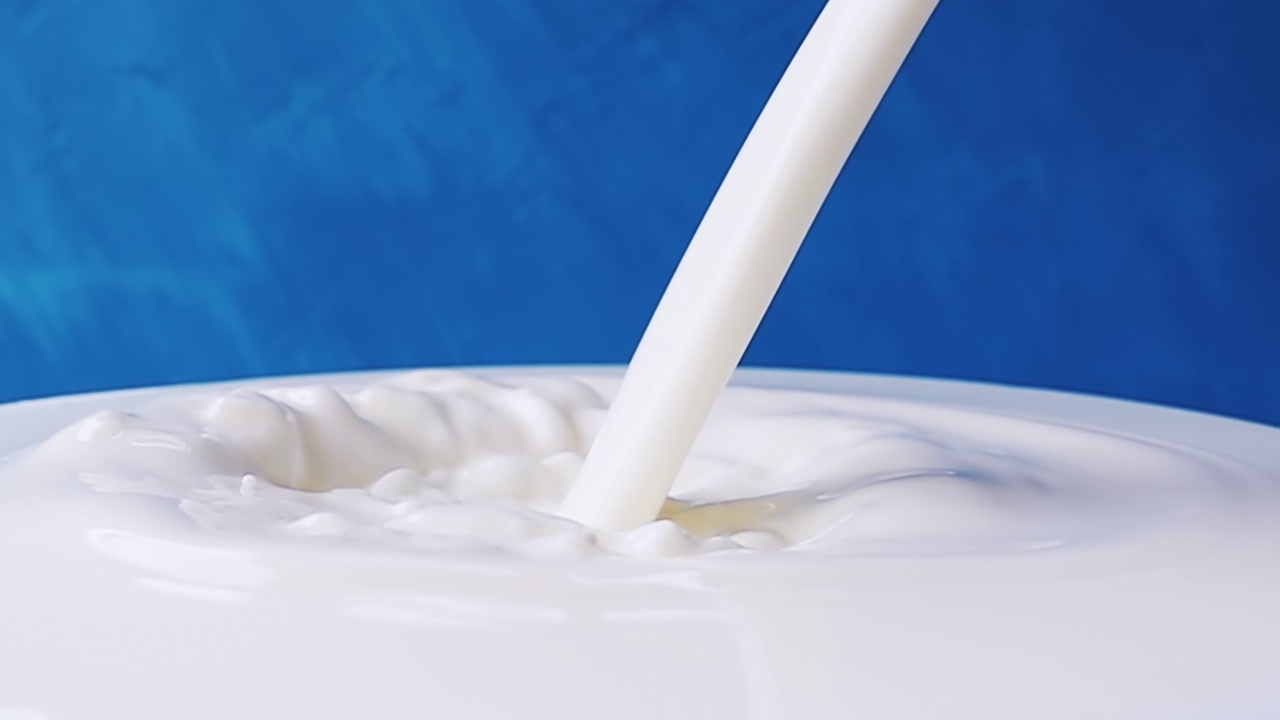 牛奶倒在牛奶表面的特写与美丽的飞溅和滴在蓝色的背景。带有速度斜坡效果的4k原始慢动作视频。用高速电影摄影机拍摄，1000帧/秒。视频素材