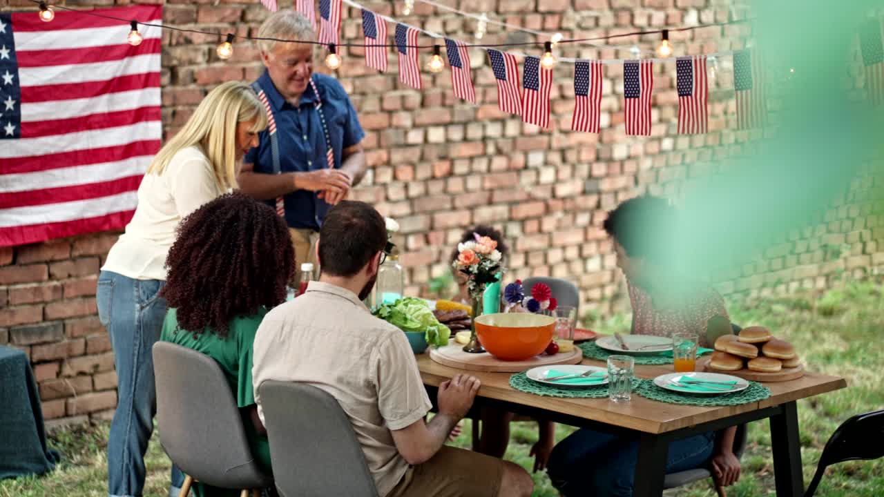 快乐的多民族家庭在7月4日户外聚会的餐桌上等待汉堡视频素材