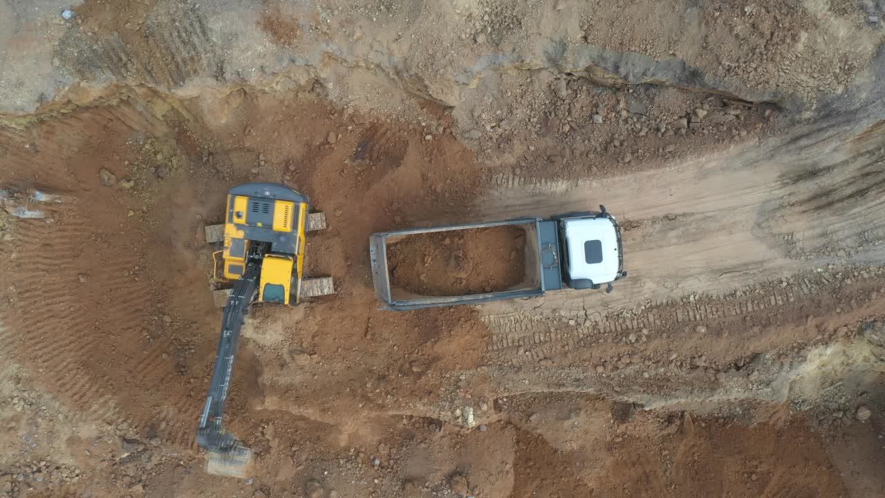 航拍现场采矿场地。无人机飞过挖土机挖土并将土装载到自卸卡车上。建筑施工中的土方搬运设备。重工业的概念。俯视图视频素材