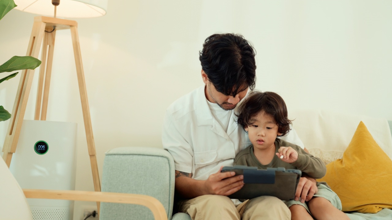 快乐亚洲父子在家里一起使用平板电脑。视频素材