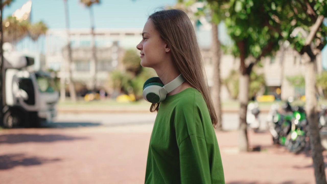 戴着耳机的快乐女人走在阳光明媚的城市视频素材
