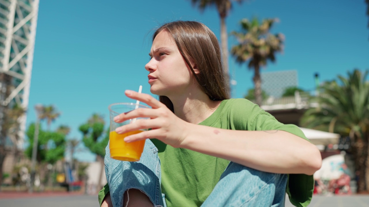 阳光明媚的女人四处张望，喝着果汁视频素材